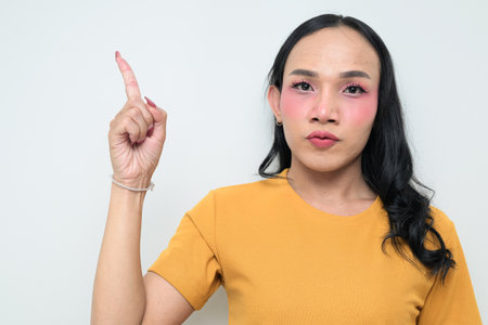 Studio portrait of a young Thai transgender individual with makeup and long hair. Concept of gender expression, LGBTQ pride, and inclusivity showing authentic beauty and diversity.の写真素材