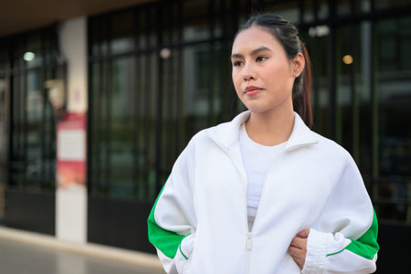 Happy young Asian woman in sporty activewear outdoors. Casual lifestyle portrait with cheerful expression, natural light, and positive energy for wellness, vitality, and fitness themes.の写真素材