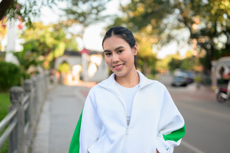 Happy young Asian woman in sporty activewear outdoors. Casual lifestyle portrait with cheerful expression, natural light, and positive energy for wellness, vitality, and fitness themes.の写真素材