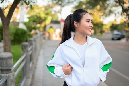 Happy young Asian woman in sporty activewear outdoors. Casual lifestyle portrait with cheerful expression, natural light, and positive energy for wellness, vitality, and fitness themes.の写真素材