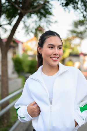 Happy young Asian woman in sporty activewear outdoors. Casual lifestyle portrait with cheerful expression, natural light, and positive energy for wellness, vitality, and fitness themes.の写真素材