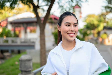 Happy young Asian woman in sporty activewear outdoors. Casual lifestyle portrait with cheerful expression, natural light, and positive energy for wellness, vitality, and fitness themes.の写真素材