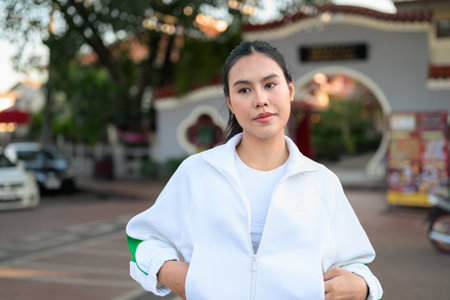 Happy young Asian woman in sporty activewear outdoors. Casual lifestyle portrait with cheerful expression, natural light, and positive energy for wellness, vitality, and fitness themes.の写真素材