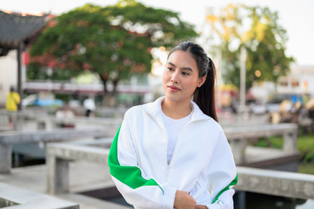 Happy young Asian woman in sporty activewear outdoors. Casual lifestyle portrait with cheerful expression, natural light, and positive energy for wellness, vitality, and fitness themes.の写真素材