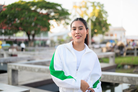 Happy young Asian woman in sporty activewear outdoors. Casual lifestyle portrait with cheerful expression, natural light, and positive energy for wellness, vitality, and fitness themes.の写真素材