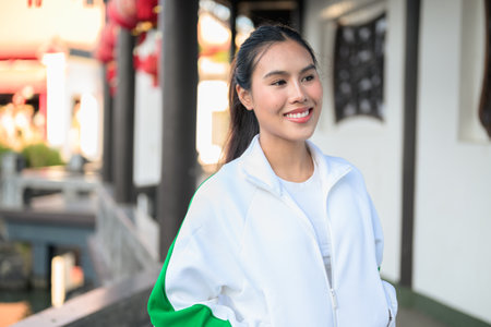 Happy young Asian woman in sporty activewear outdoors. Casual lifestyle portrait with cheerful expression, natural light, and positive energy for wellness, vitality, and fitness themes.の写真素材