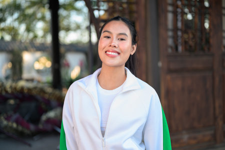 Happy young Asian woman in sporty activewear outdoors. Casual lifestyle portrait with cheerful expression, natural light, and positive energy for wellness, vitality, and fitness themes.の写真素材