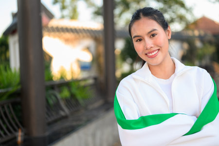 Happy young Asian woman in sporty activewear outdoors. Casual lifestyle portrait with cheerful expression, natural light, and positive energy for wellness, vitality, and fitness themes.の写真素材