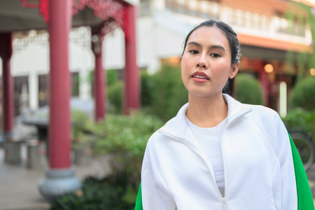 Happy young Asian woman in sporty activewear outdoors. Casual lifestyle portrait with cheerful expression, natural light, and positive energy for wellness, vitality, and fitness themes.の写真素材
