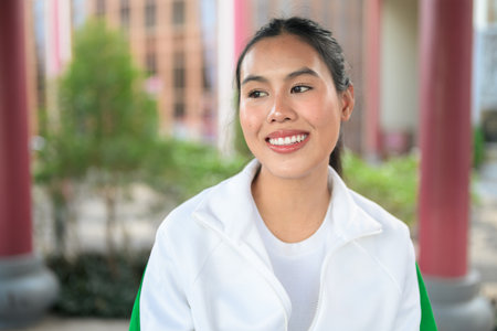 Happy young Asian woman in sporty activewear outdoors. Casual lifestyle portrait with cheerful expression, natural light, and positive energy for wellness, vitality, and fitness themes.の写真素材