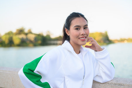 Happy young Asian woman in sporty activewear outdoors. Casual lifestyle portrait with cheerful expression, natural light, and positive energy for wellness, vitality, and fitness themes.の写真素材