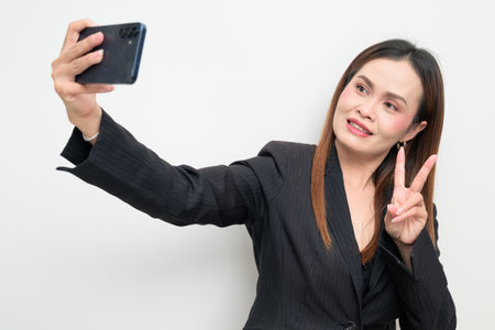 Studio portrait of an Asian business woman wearing a black blazer against a white background using phone. Professional and confident look suitable for corporate, office, career, and workplace themes.の写真素材