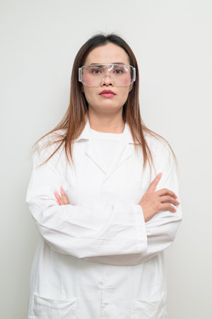 Studio portrait of an Asian scientist wearing a white lab coat and protective glasses. Serious, professional look suitable for laboratory, research, science, medical, and clinical themes.の写真素材