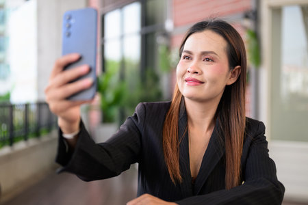 Outdoor portrait of a confident Thai businesswoman in a black blazer, taking a break in a modern office common area, exuding professionalism and leadershipの写真素材