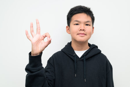 Studio portrait of an Asian teenage boy standing against a plain white background wearing black hoodie. Simple look suitable for youth, education, family, and lifestyle themes.の写真素材