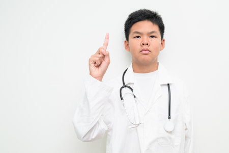 Portrait of a young Asian boy wearing a white lab coat and stethoscope. Suitable for healthcare, medical education, children profession dreams, and future doctor concepts.の写真素材