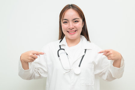 Portrait of young Asian female doctor against white background wearing lab coat and stethoscopeの写真素材