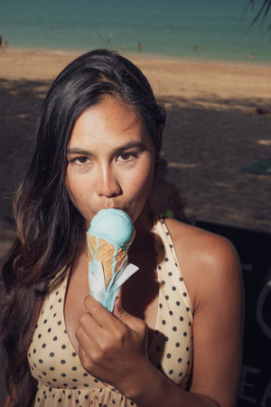 Close-up portrait of happy Asian woman holding melting ice cream on sunny beach