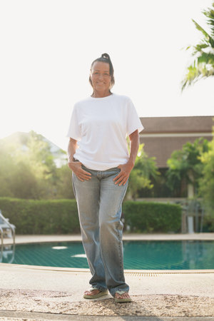 Happy mature Scandinavian woman standing near swimming pool in tropical outdoor settingの写真素材