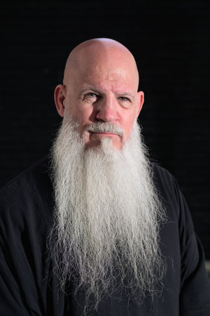 Detailed head-and-shoulders portrait of a bald man with a long white beard against a dark background