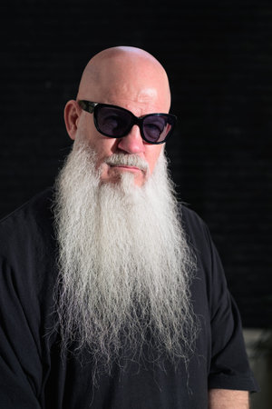 Detailed head-and-shoulders portrait of a bald man with a long white beard against a dark background