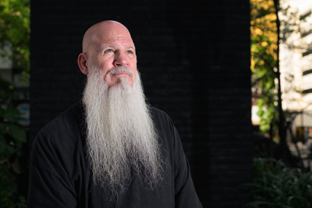 Detailed head-and-shoulders portrait of a bald man with a long white beard against a dark background