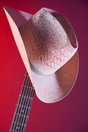 A red electric guitar and straw hat isolated against a red spotlight background in the vertical format.の写真素材