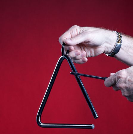 A musical triangle being played by hands isolated against a red background in the square format with copy space.の写真素材