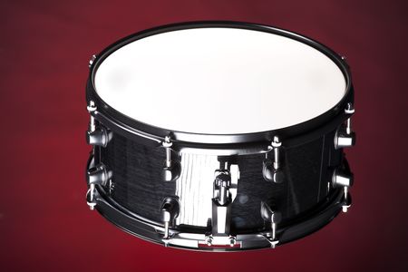 A black metallic wood finish snare drum isolated against a dark red background in the horizontal format.の写真素材