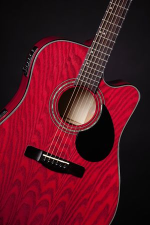 A red acoustic electric guitar isolated against a black background in the vertical format.の写真素材