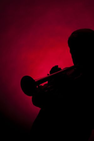 A senior male man trumpet player performer in silhouette isolated against a spotlight red background.の写真素材
