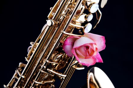 A pink rose mounted on a gold brass saxophone isolated against a black background in the horizontal format.の写真素材