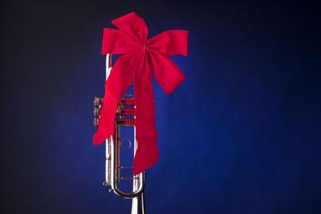 A silver trumpet or cornet horn with a red ribbon bow isolated against blue background.の写真素材