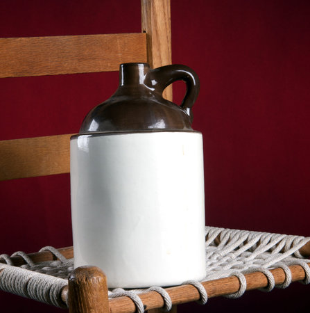 An old pottery ceramic country jug and rope bottom chair on a red background in the square format.