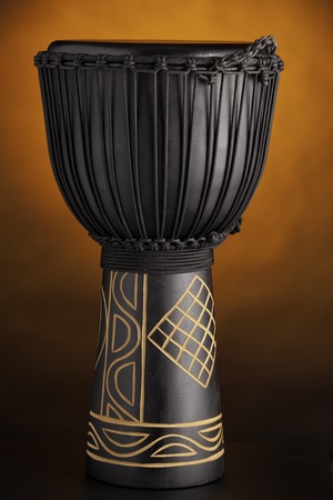 A black djembe conga drum isolated against a yellow or gold spotlight background.の写真素材