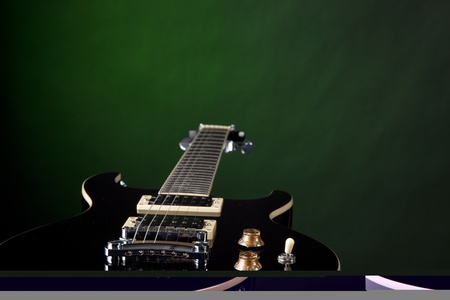 A jet black electric guitar isolated against a spotlight green background with copy space.の写真素材