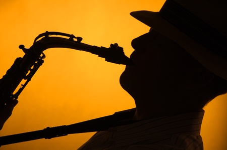 A saxophone player with a hat in silhouette against a stage light gold or yellow background in the horizontal format with copy space.の写真素材