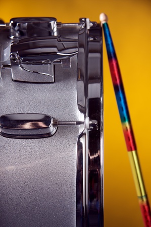 A silver sparkle snare drum with sticks against a gold or yellow background in the vertical format.の写真素材