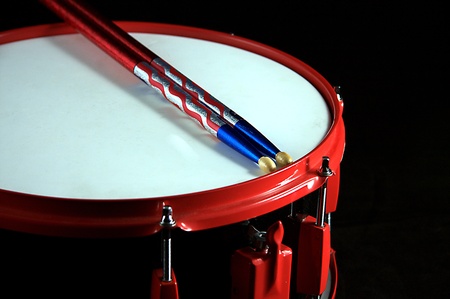 A red and black colored snare drum with flag colored sticks against a black background in the horizontal format.の写真素材