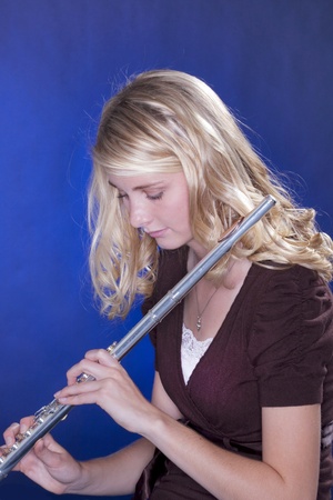 A blond teenage female girl holding a silver flute against a blue background.の写真素材