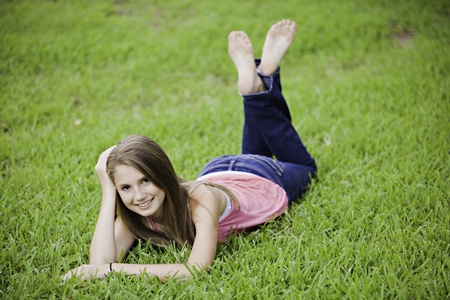 A teenage girl female lying face down on a green grass field.の写真素材