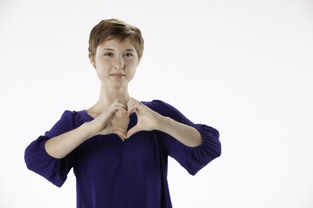 Pretty happy teenage female girl with red brown hair and purple shirt isolated has heart shaped hands the options on a white background の写真素材