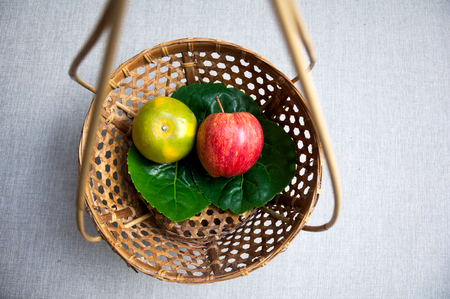 An orange and a apple on the leave putting on small wood traditional thai basketの写真素材