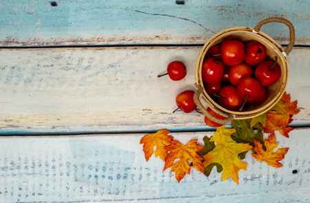Bunch of small apples in a straw basket on teal wood background. Autumn background concept for fallの写真素材