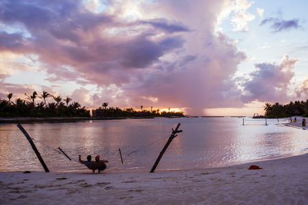 North Male Atoll, Maldives - November 23, 2019: A happy adult couple relaxes in a hammock over the water at a resort in the Maldives during sunsetのeditorial素材