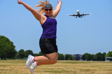 Blonde adult woman at Gravelly Point Park in Washington DC jumps as an airplane flies in for a landing at the DCA Reagan International airportの写真素材