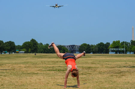 Young adult woman attempts to do a cartwheel in a park, but fails. Airplane and Washington Monument...
