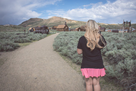 A blonde female walks on a path toward more abandoned buildings in the ghost town of Bodie Californiaの写真素材