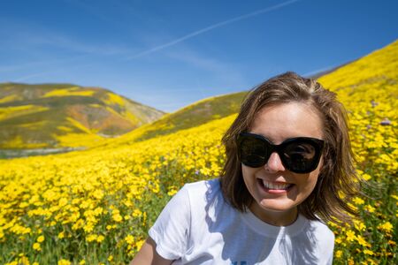 Woman wearing sunglasses sits and poses in a field of yellow wildflowers at Carrizo Plain National Monument for California superbloomの写真素材