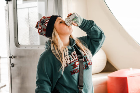 Bayfield, Wisconsin - October 19, 2019: Thirsty blonde woman tourists chugs and drinks a cup of hot...